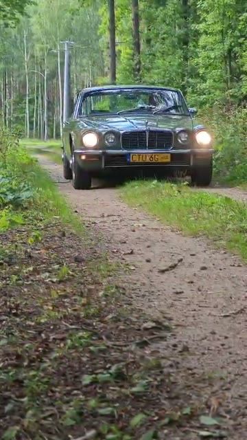 Zielony Jaguar XJ6 jedzie leśną drogą po naprawie